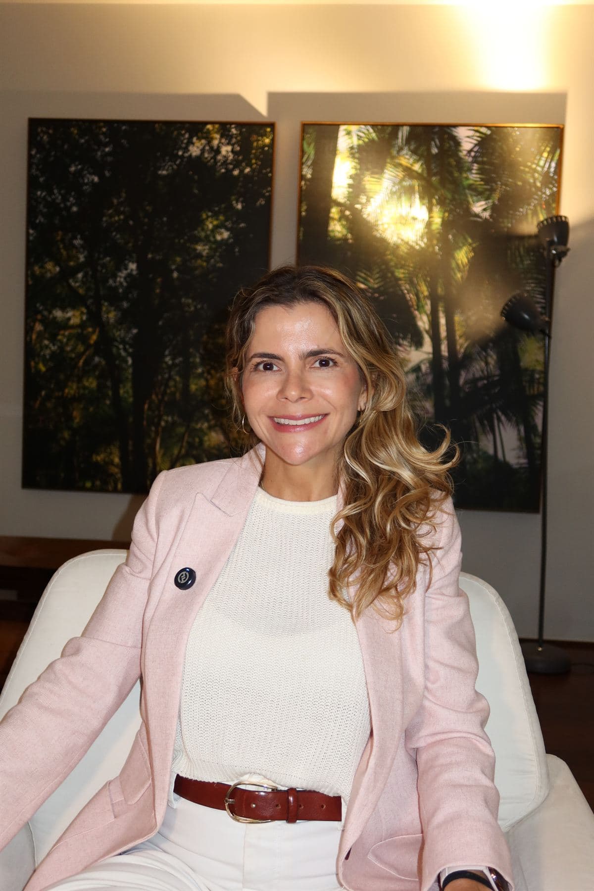 Paula Braga de blazer rosa, com fotografias de florestas ao fundo