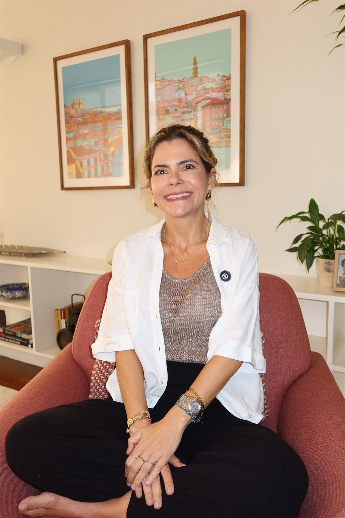 Paula Braga sorrindo em poltrona, com quadros coloridos ao fundo